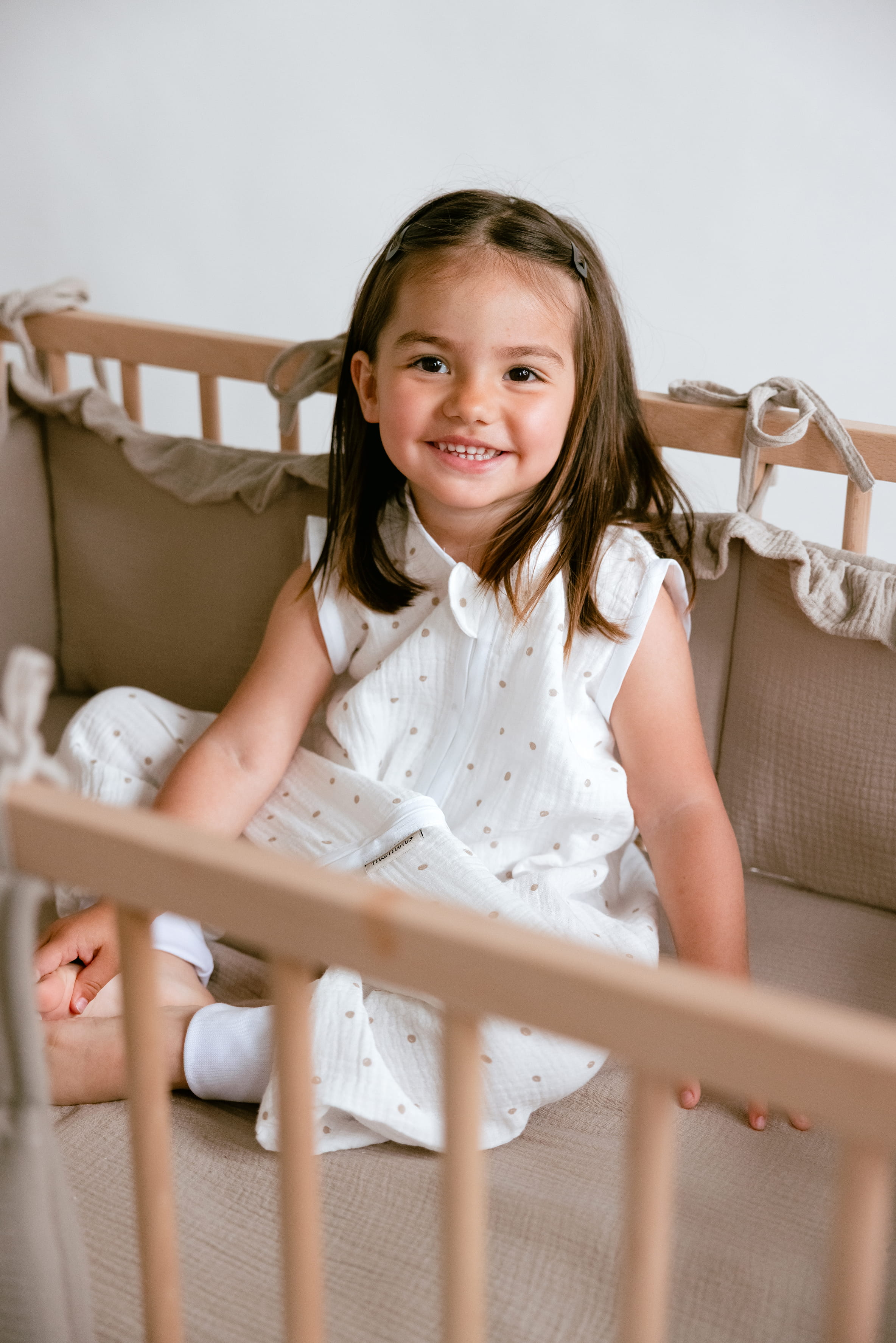 Djevojčica u bijeloj vreći za spavanje s uzorkom u dječjem krevetiću